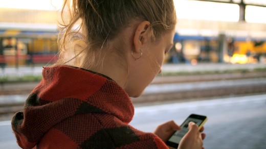En flicka som ligger och tittar på sin mobil i en soffa